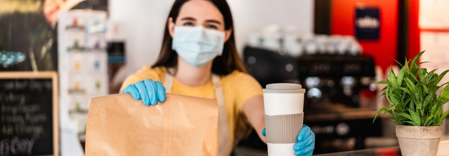 A server handling over a paper bag food take out with a cup of coffee.