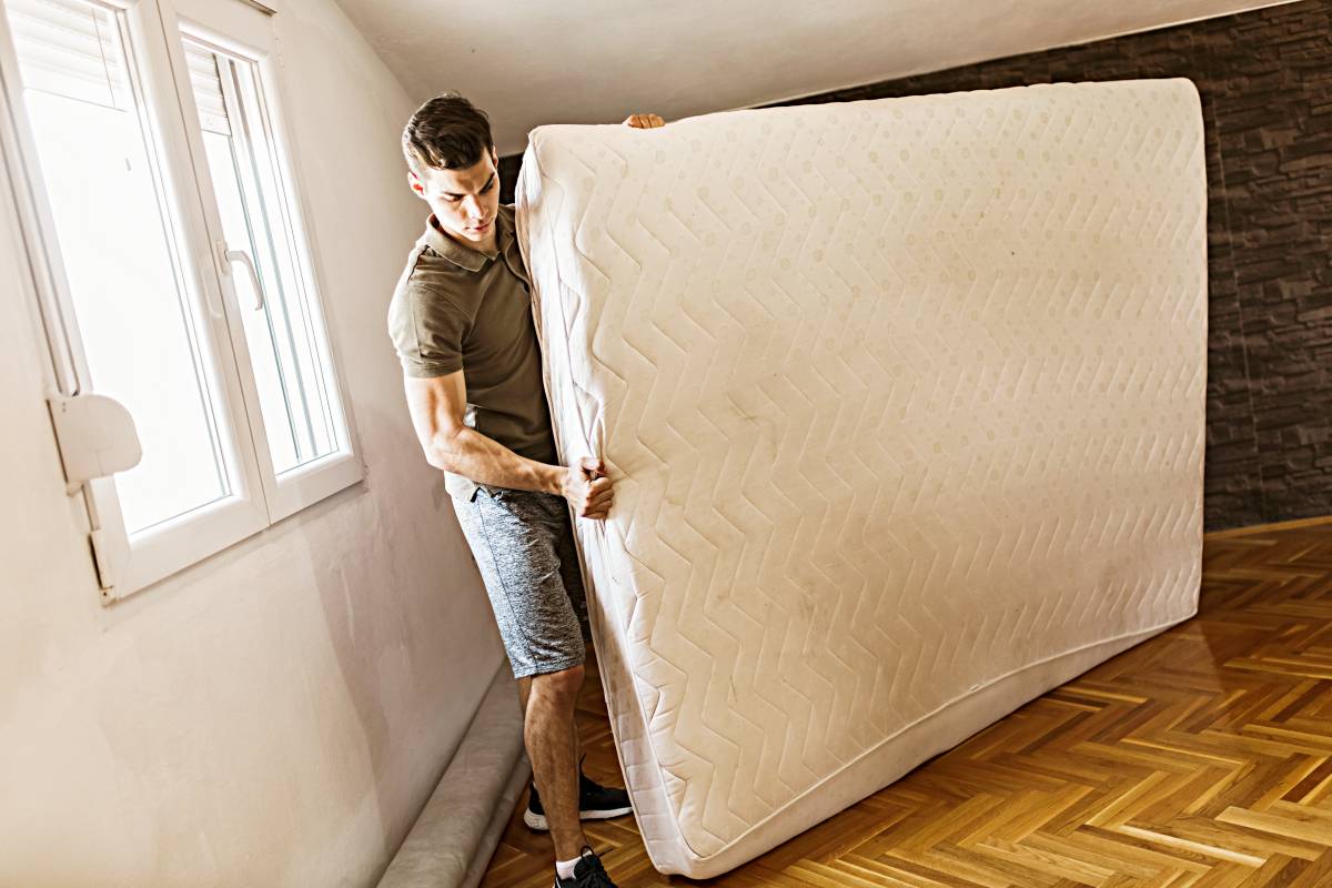 A man moving a mattress in a bedroom during relocation