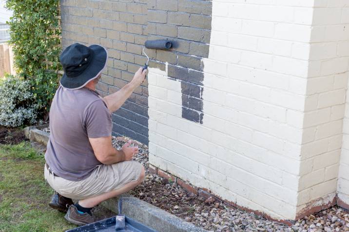 a man painting the exterior of a brick house