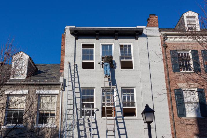 a man painting the exterior of a multi-story brick house