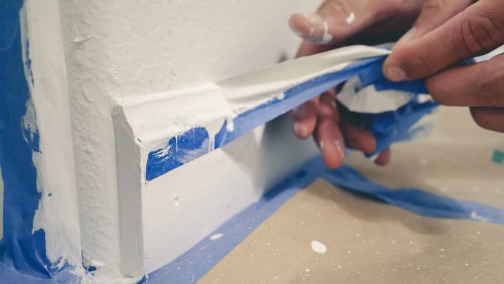 painter pulling off blue painter's tape from wall to reveal a clean edge baseboard