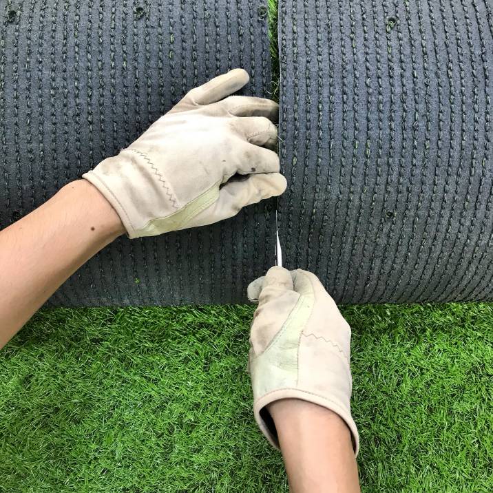 a man cutting a roll of artificial grass