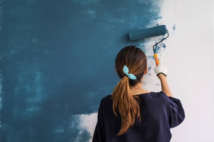 girl applying blue limewash paint on wall with a roller