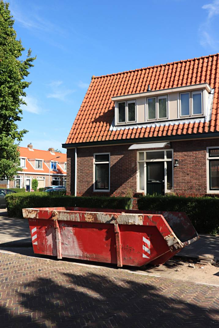 Skip bin hire cost - red skip bin in front of a residential house, ready for waste disposal