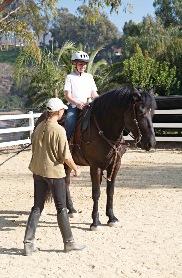 a woman teaching a kid how to ride a horse