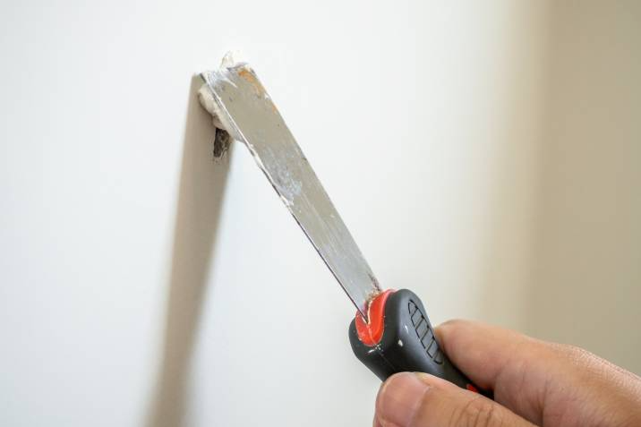 handyman repairing a crack on a white drywall, plasterboard with spatula