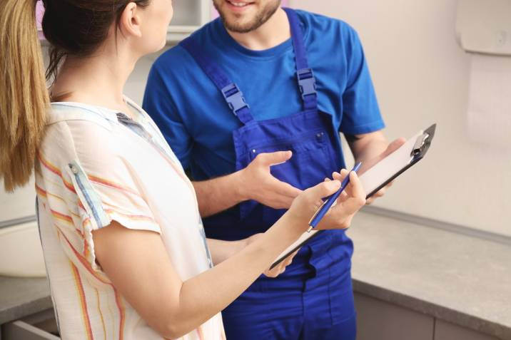 Smiling handyman in uniform talking to client indoors