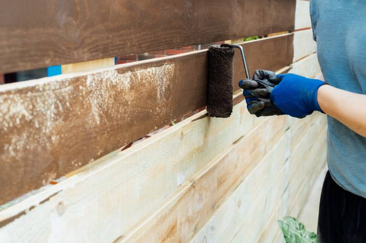 a handyman painting a wooden board fence with a roller