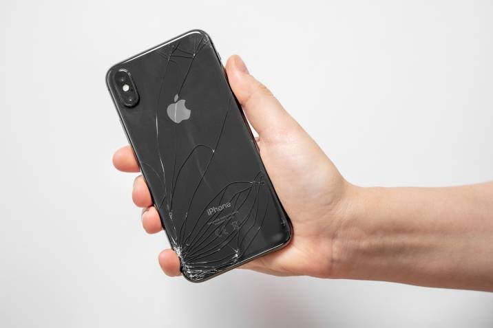 a man holding a damaged iPhoneiPhone repair cost - A person holding an iPhone with a severely cracked back glass, highlighting the need for professional repair.