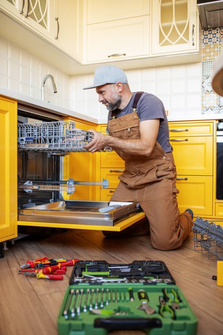 a repairman using tools to repair a dishwasher