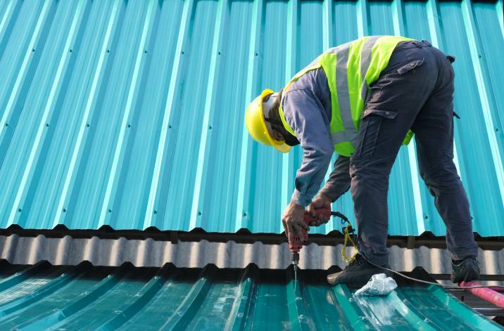 a worker using an electric drill to install a metal roof