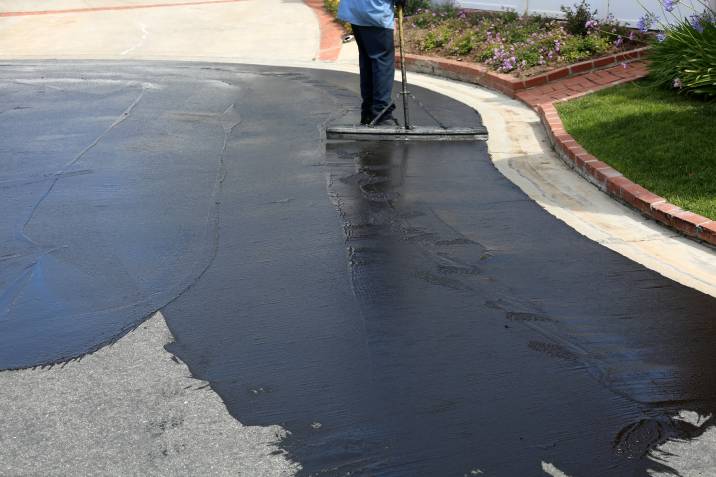 Asphalt driveway cost - contractor stirring asphalt sealant before application