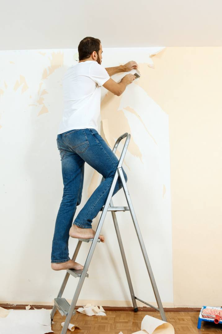 a casually dressed man removing white wallpaper