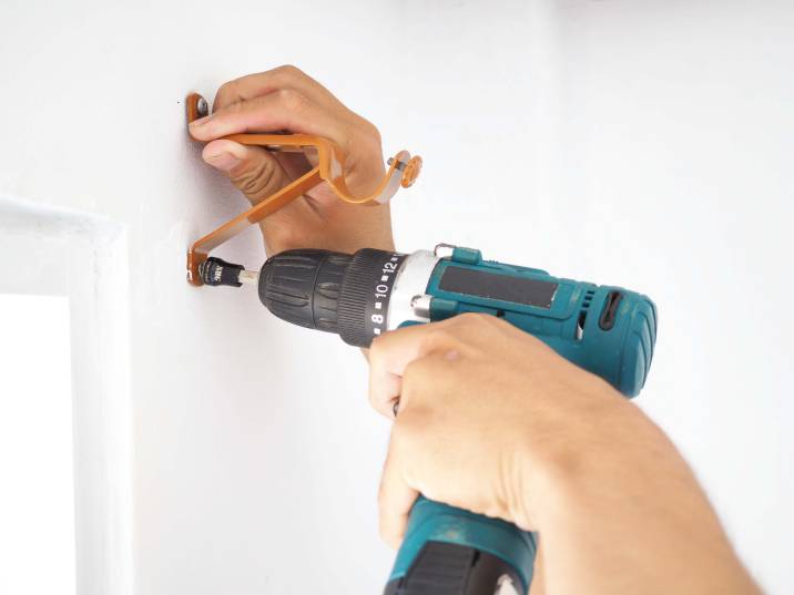 Closeup hands. Drilling screws to install curtain rod brackets