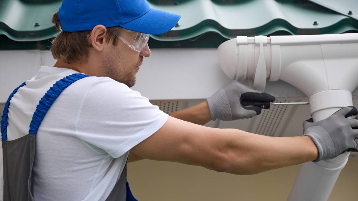 worker installing a new gutter under a metal tiled roof