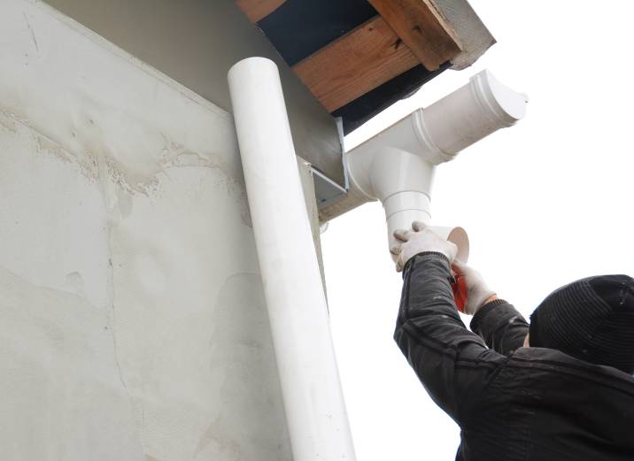a roofer installing a gutter system with drain downspout pipe