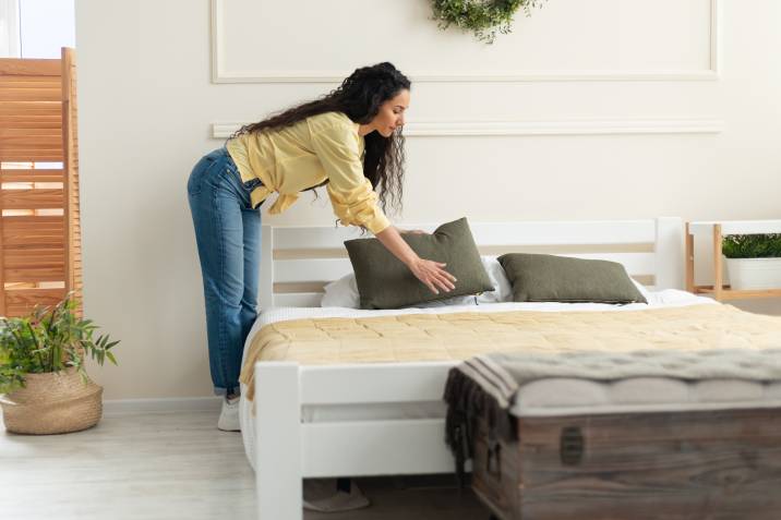 Woman making bed, holding pillow. Preparing extra room for renting out