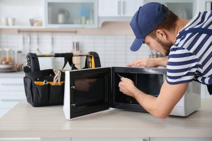 Young man electrician repairing microwave oven on kitchen counter