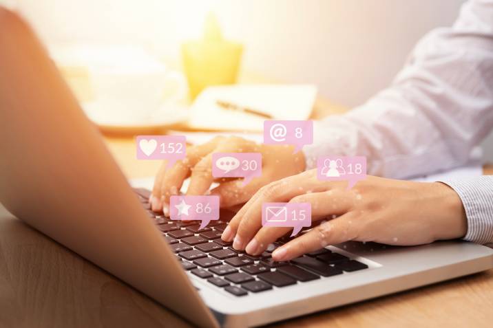Person using laptop for social media interactions with notification icons from customer in social network with like, message, email, mention and star above screen