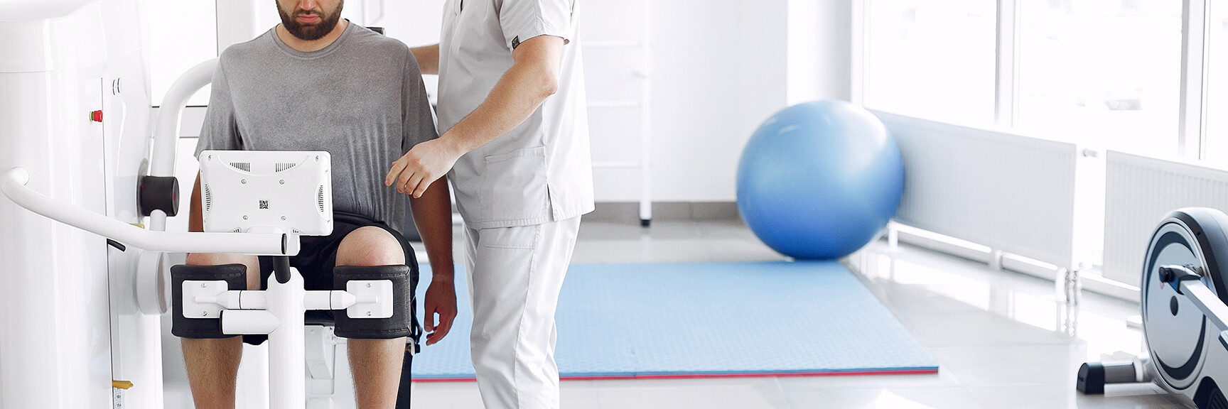 A person in an exercise maching working with an occupational therapist, using a therapy ball to improve their mobility and strength.