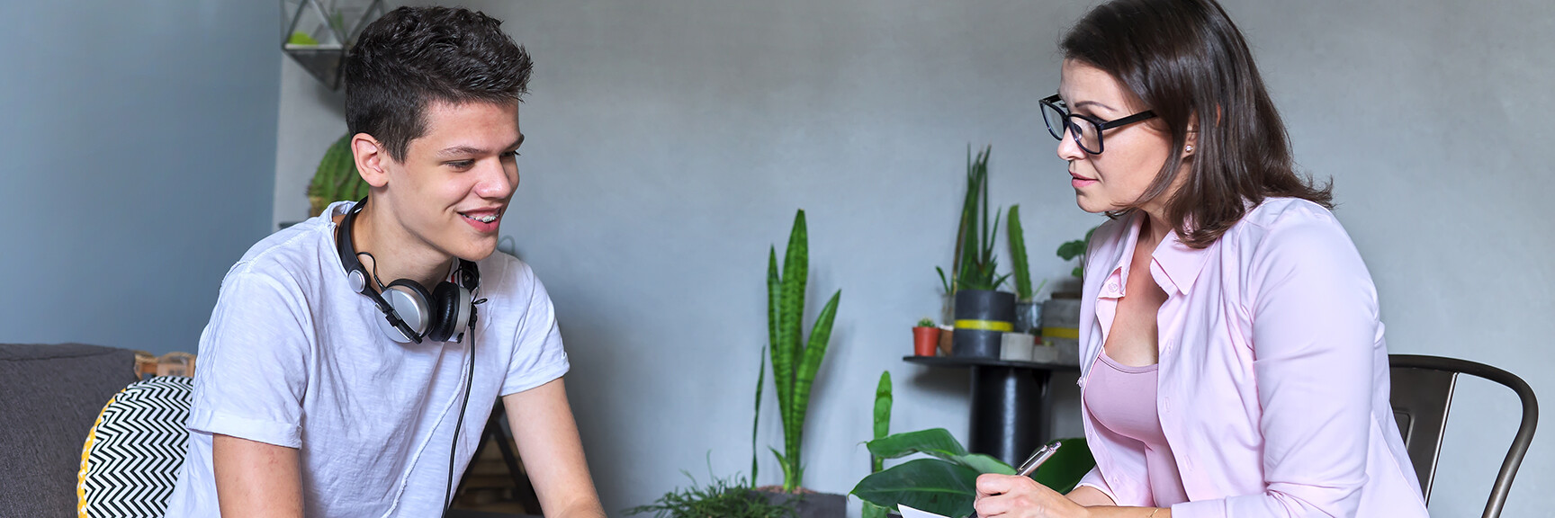 A teenager sitting on a couch in a counseling session, talking to a therapist, with a calm and supportive atmosphere.