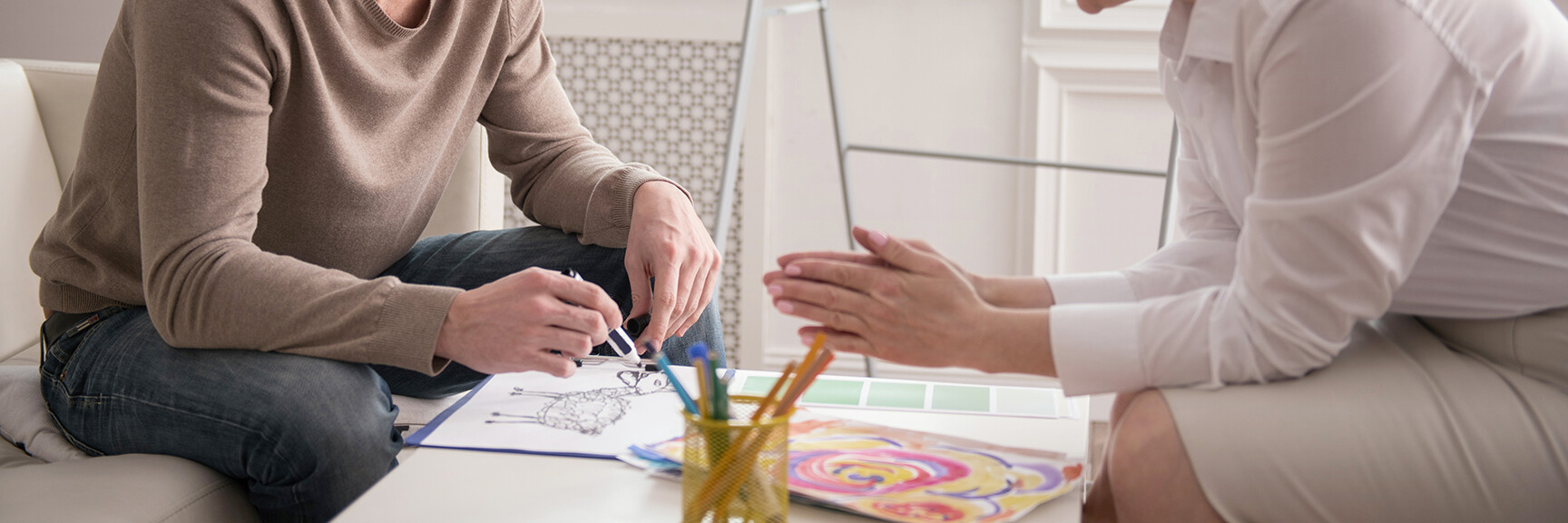 A person sitting at a table, surrounded by art supplies, creating a colorful painting as a form of therapy.