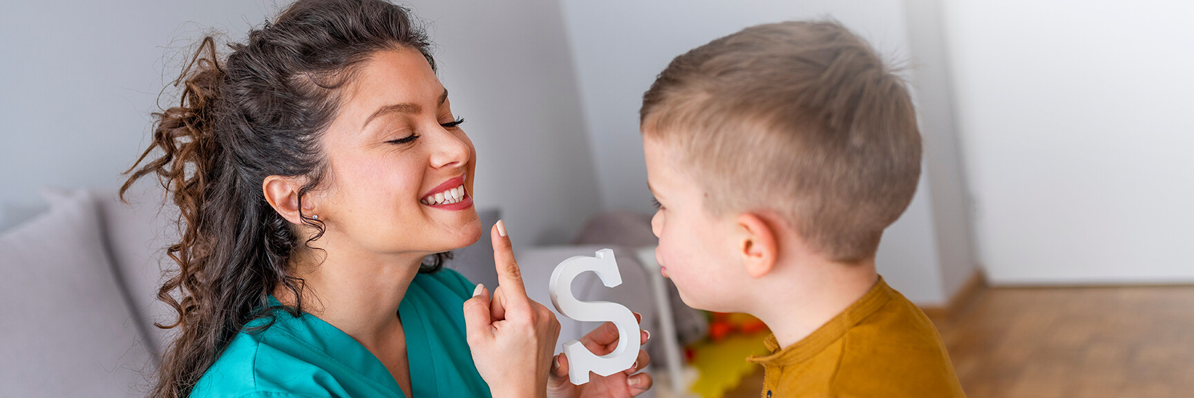 A woman teaching a kid how to pronounce the letter S.