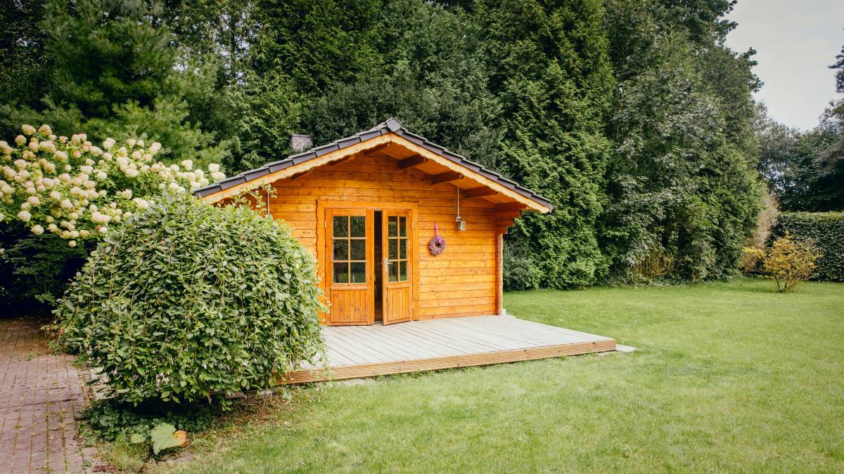 A compact black garden shed from Easyshed, positioned in a lush backyard garden with raised vegetable beds and green foliage