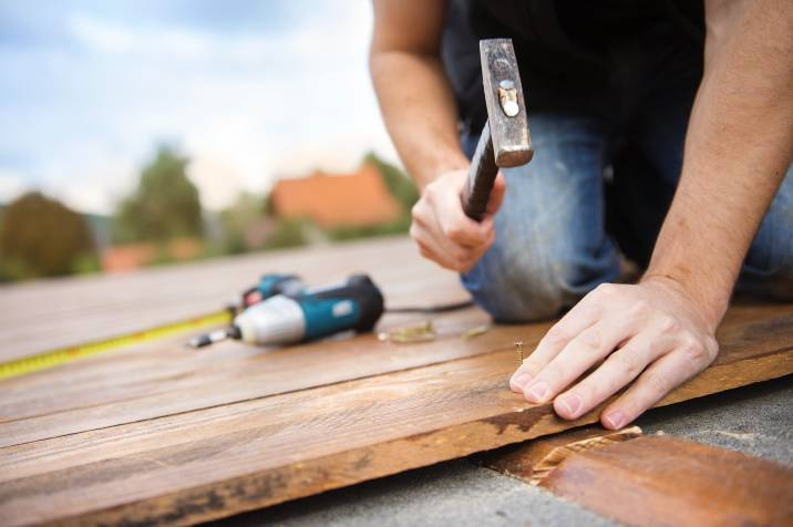 handyman nailing down wooden deck flooring