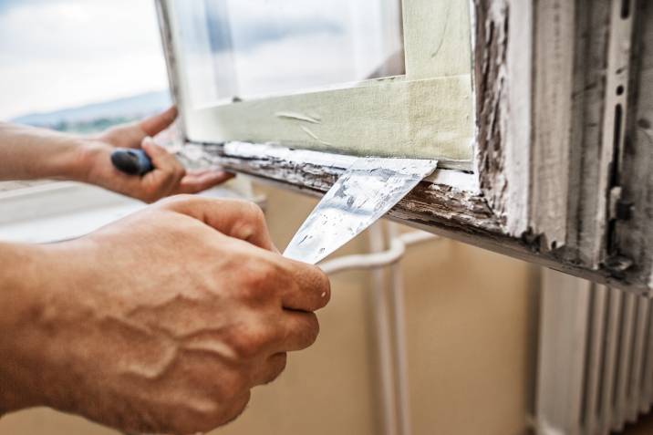 person scraping the putty off a window