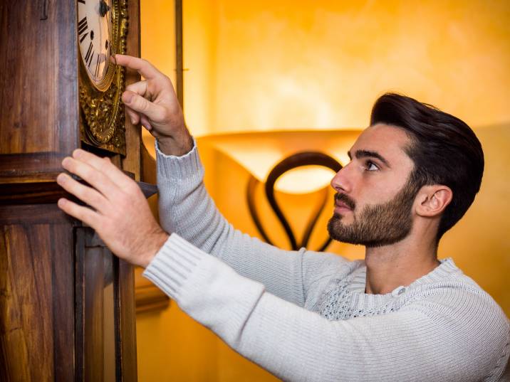 man adjusting the time on a grandfather clock