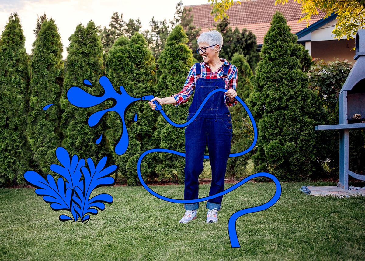 Grey-haired lady with a garden hose, watering her garden.