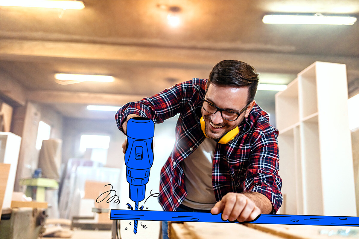 A handyman wearing a red checkered shirt using a drill.