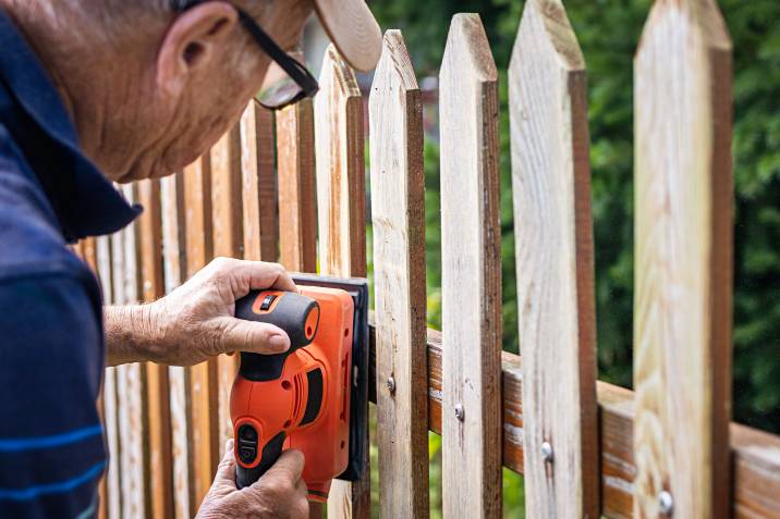 a man sanding a picket fence