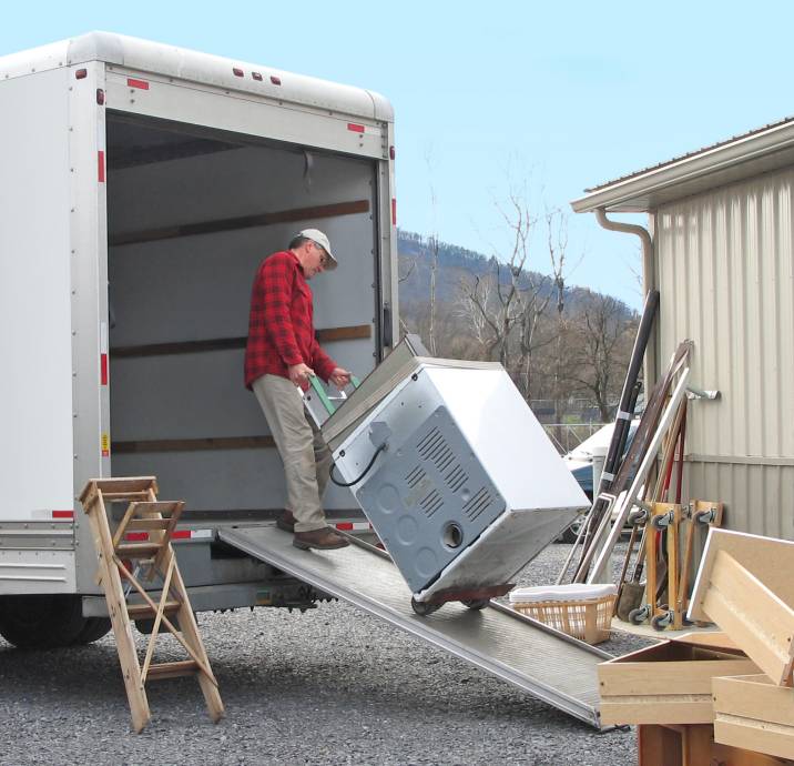man loading a truck with a stove using a dolly