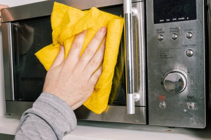 a-person-wiping-the-microwave-oven-clean