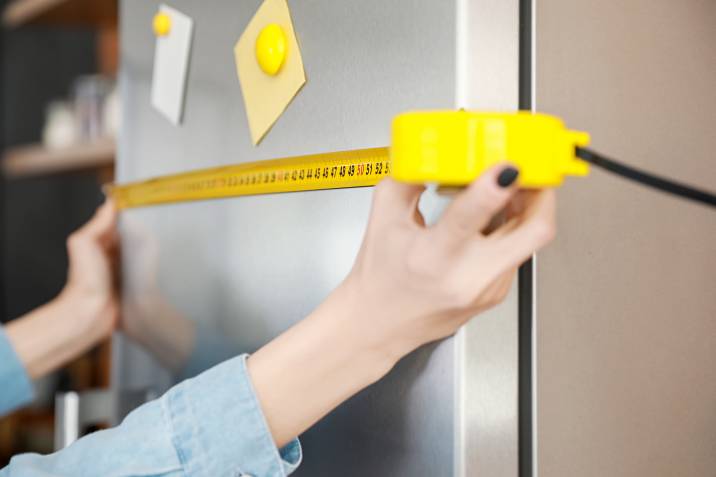 a woman measuring the width of a fridge