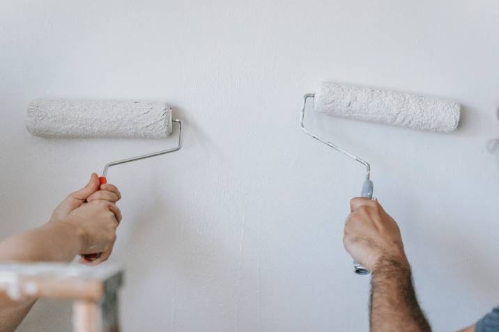 Two people painting a wall with eggshell finish, closeup of hands holding roller brush