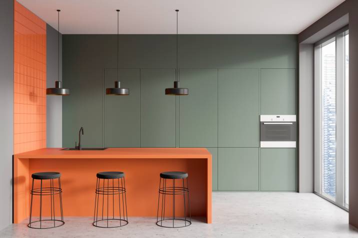 Olive green and tangerine kitchen. Bar counter with three bar stools, oven, and sink. Panoramic window with skyscraper view 