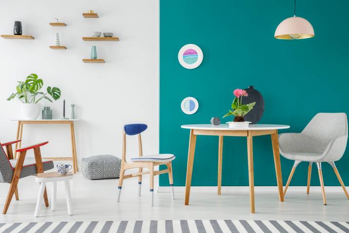 Teal and white living room wall. Pastel lamp above grey armchair at wooden table