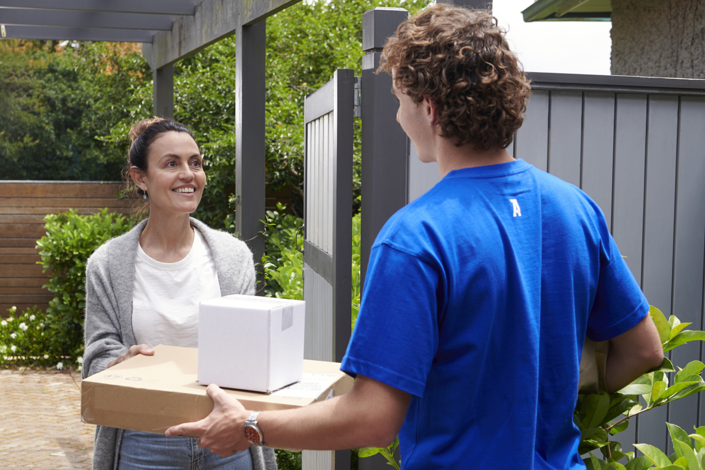 A delivery person handing a package to a receipient, walking towards a house with a smile on their face.