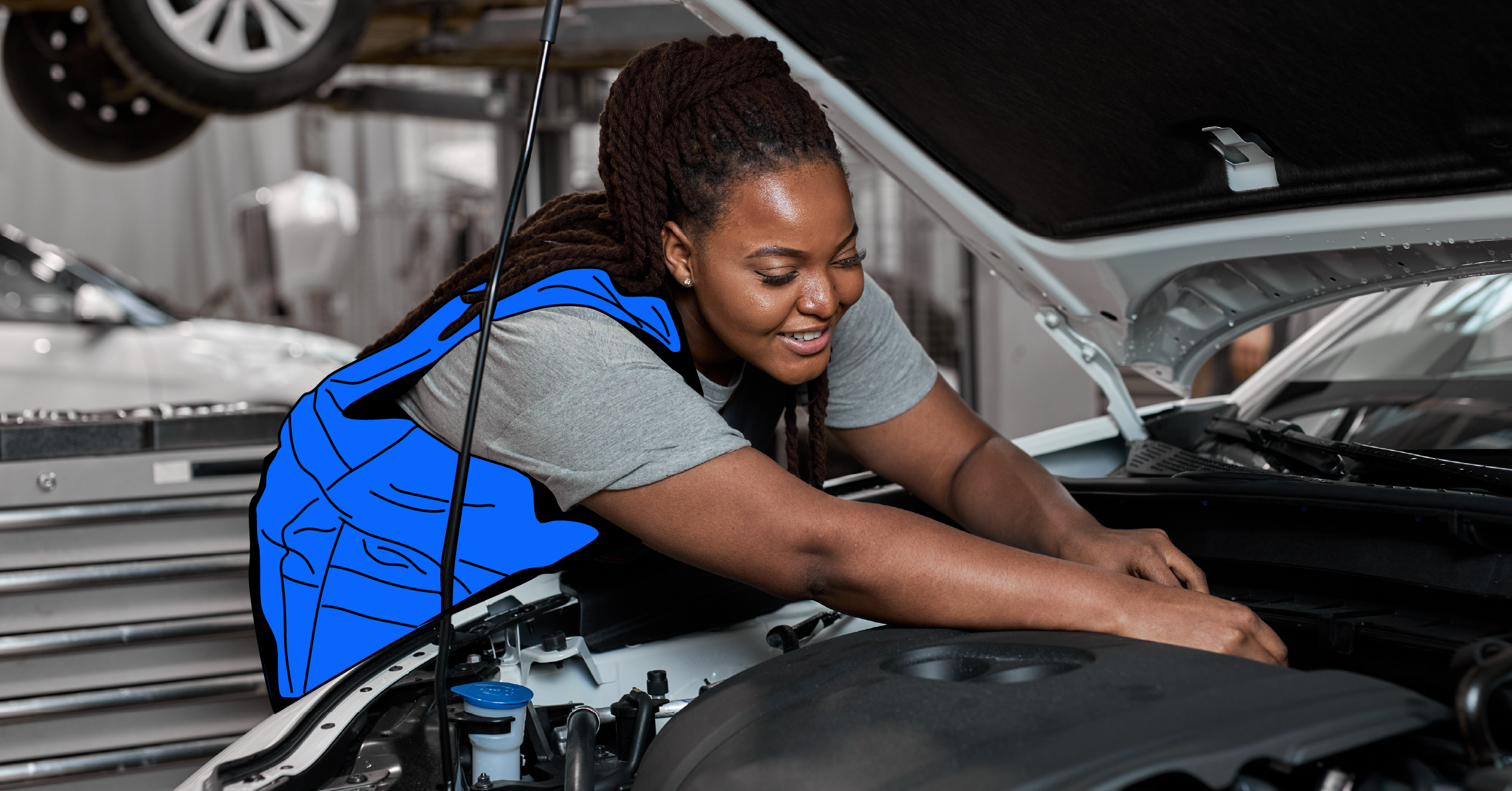 Skilled mechanic in uniform working under the hood of a car in a well-equipped garage.