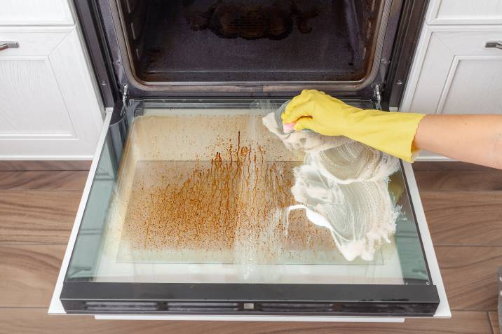 Cleaning dirty oven door with soap and sponge