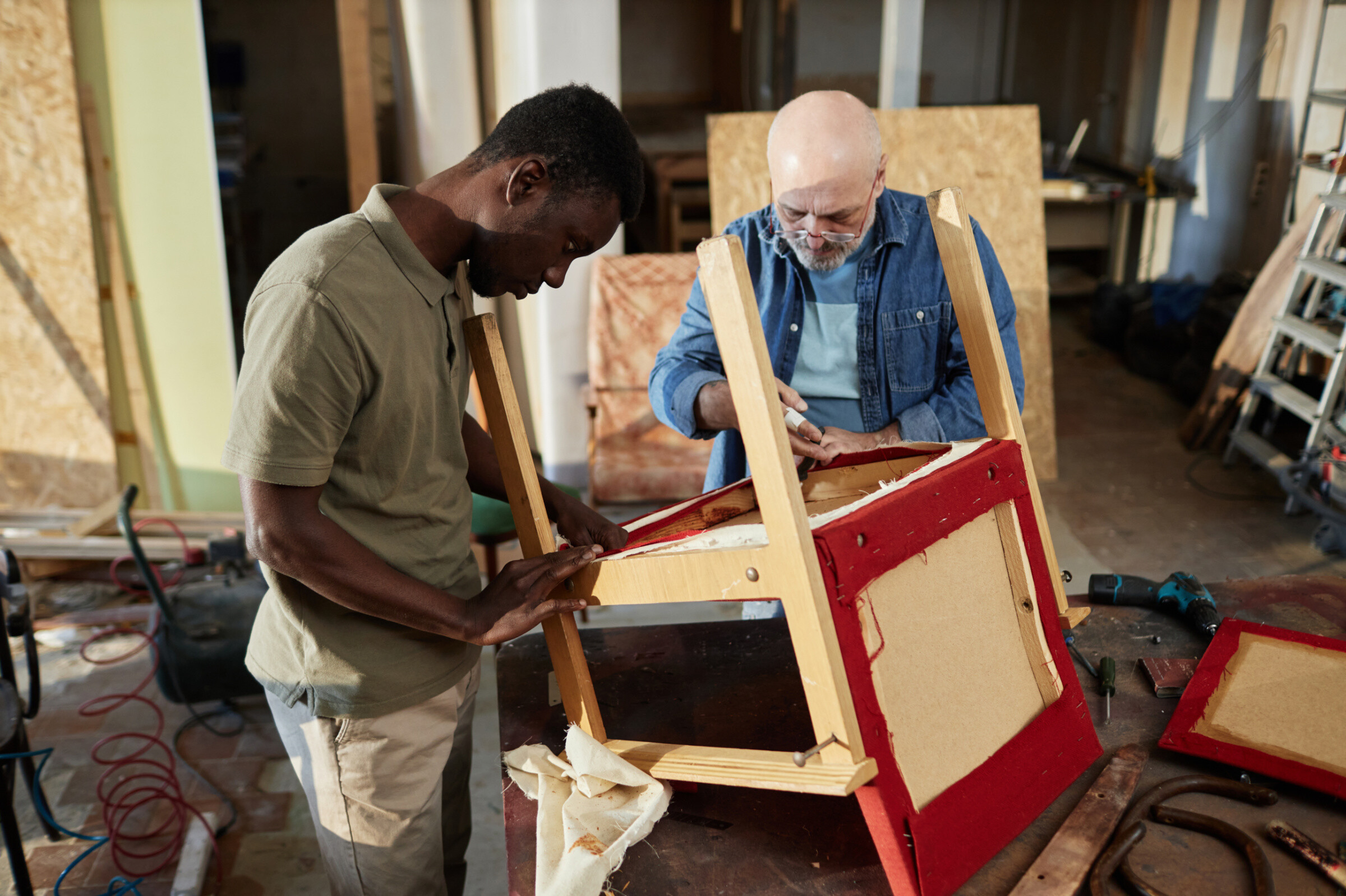 Two furniture repair experts working on a chair together in their workshop.