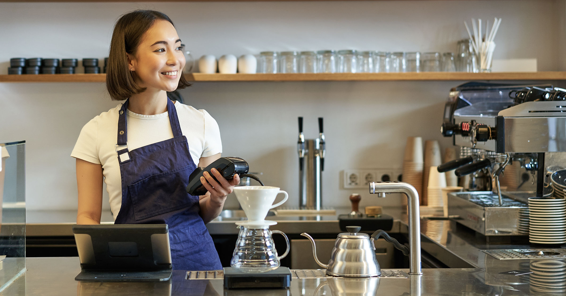 A female barista at the bar holding a payment terminal with a nice smile on her face.