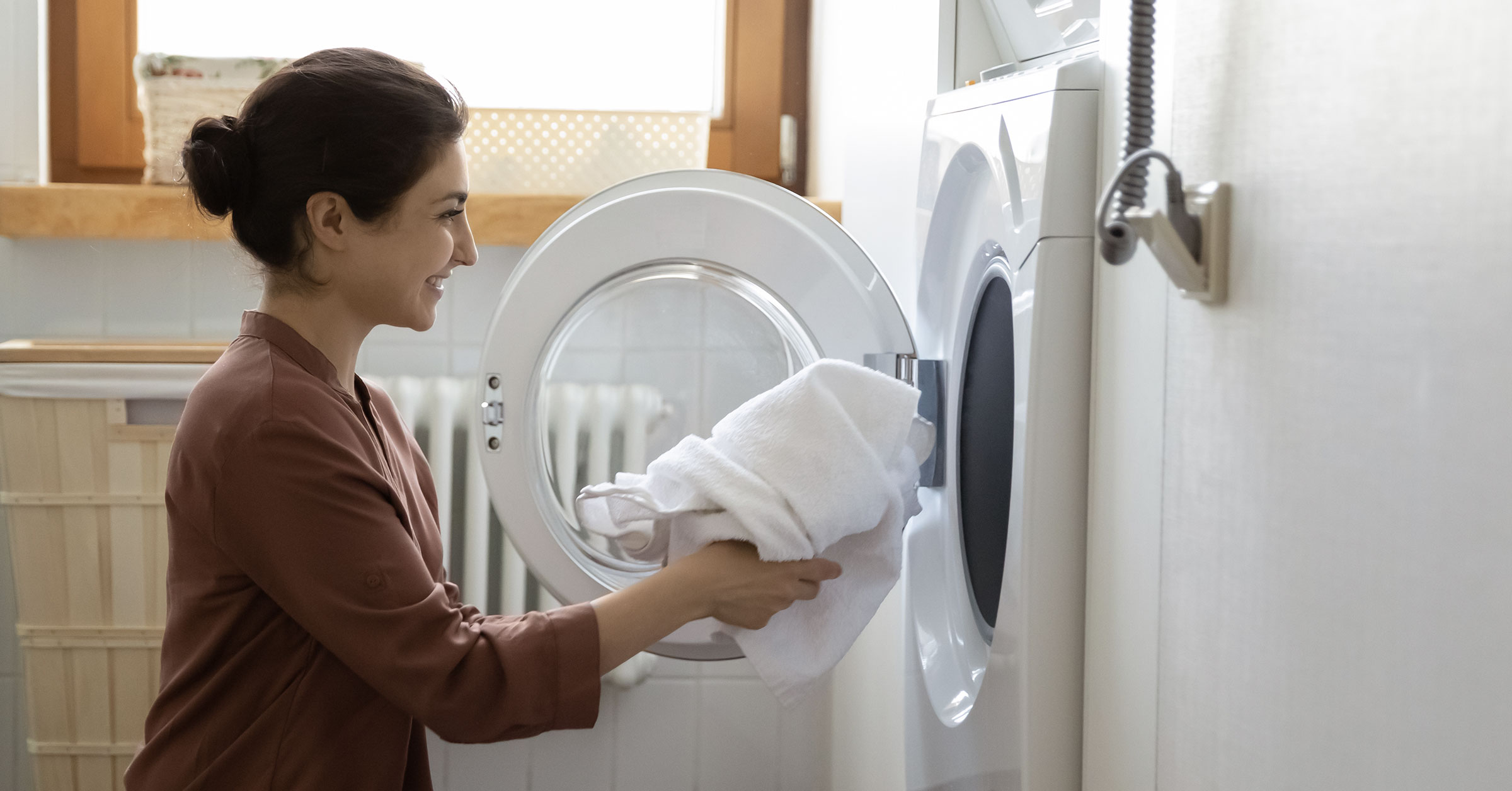 A lady smiling while placing dirty towels in a washing machine.
