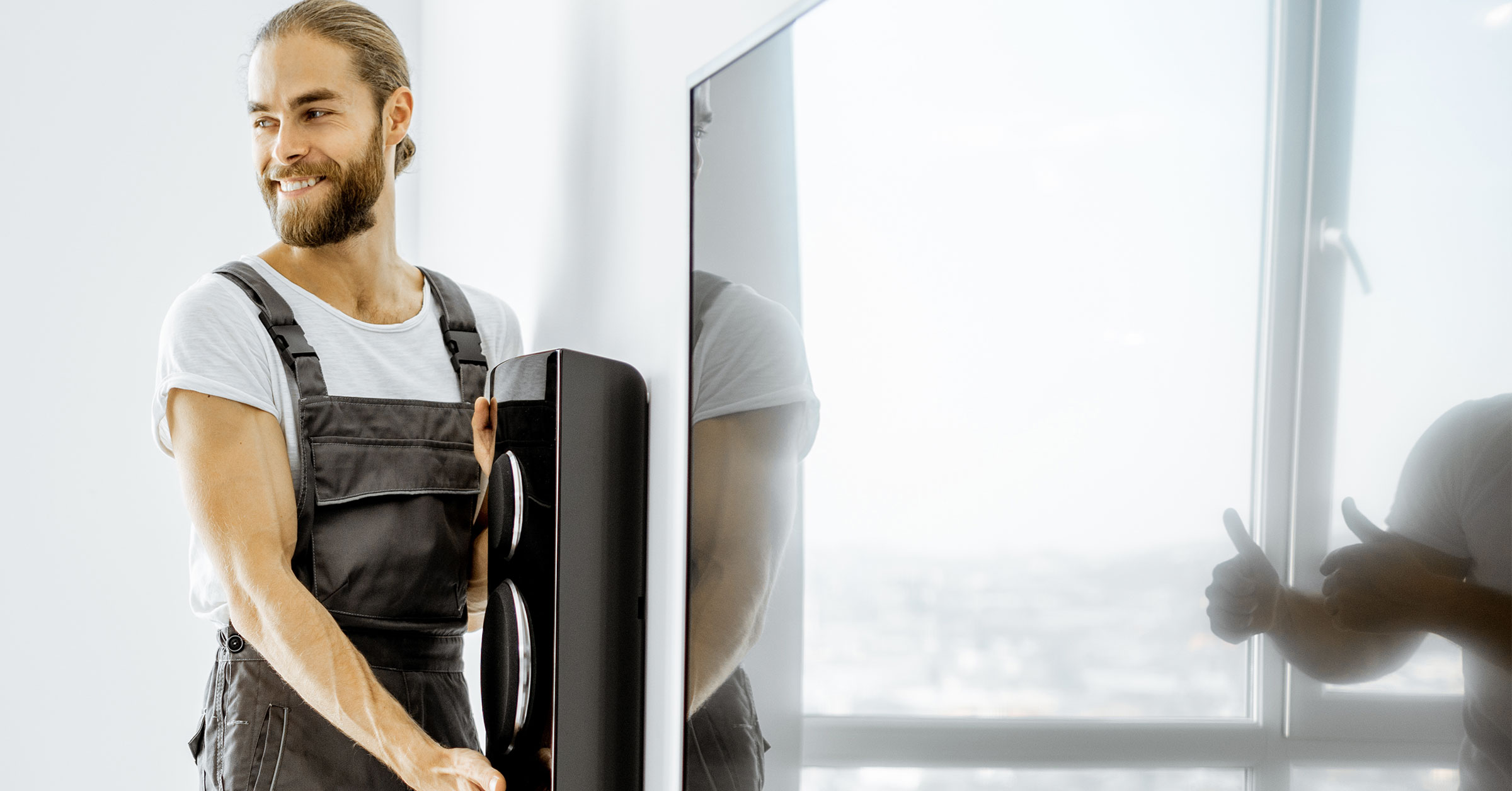 A bearded handyman installing a home theatre system that includes a large TV and speakers.