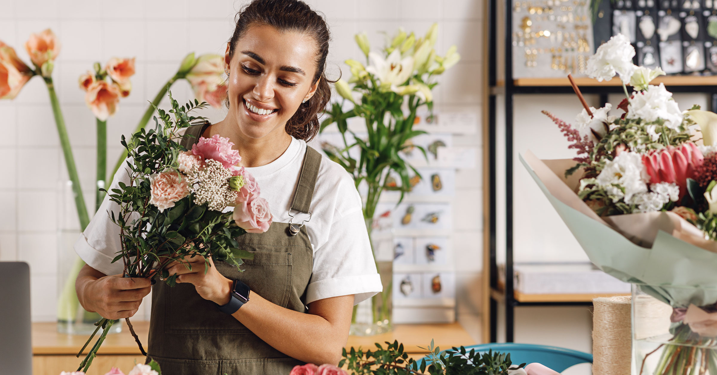 A pretty florist enthusiastically working on a bouquet of roses in a well lit and organised workshop.