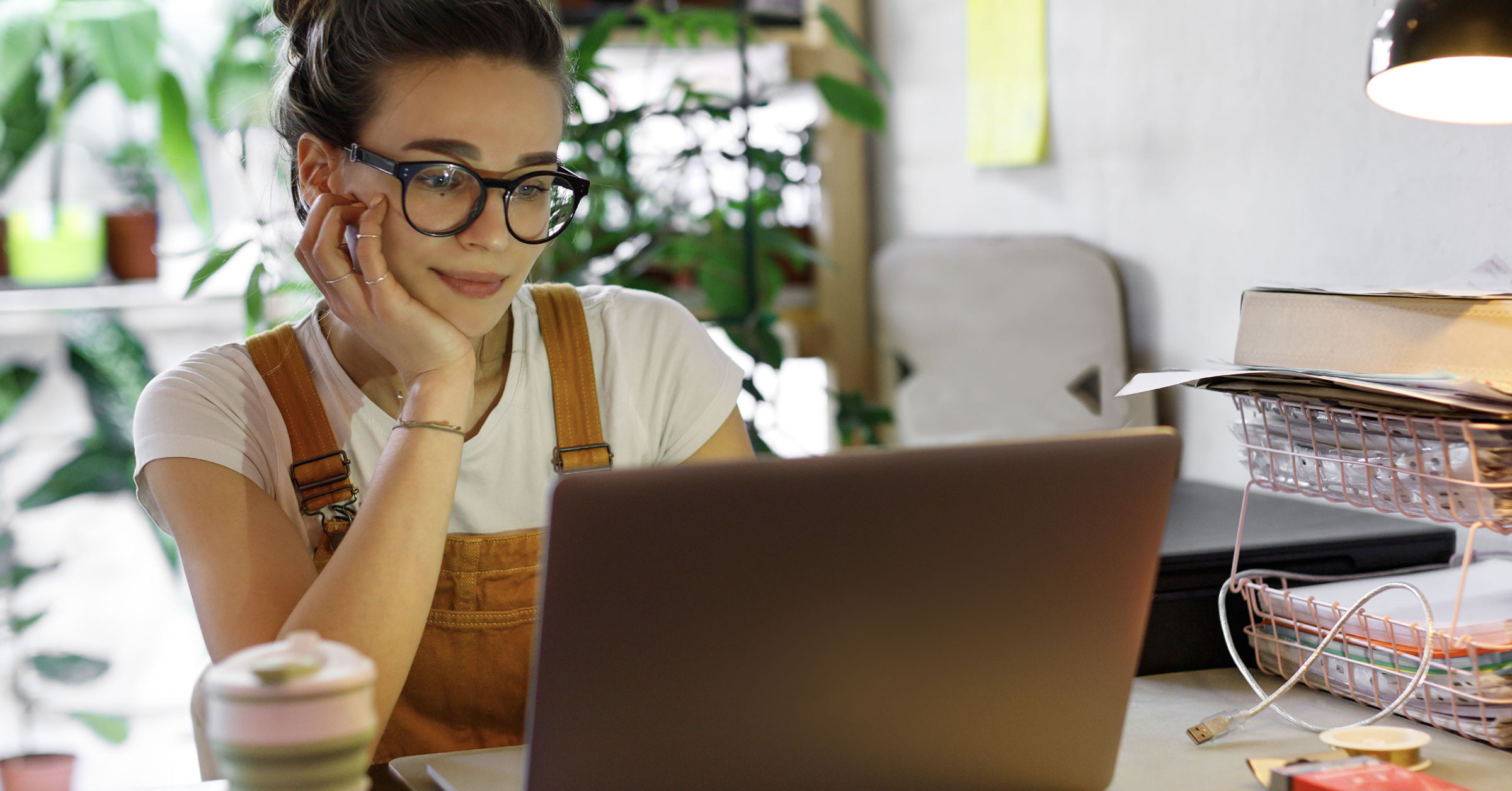 A photo of a female designer wearing glasses, working on her computer at her desk.