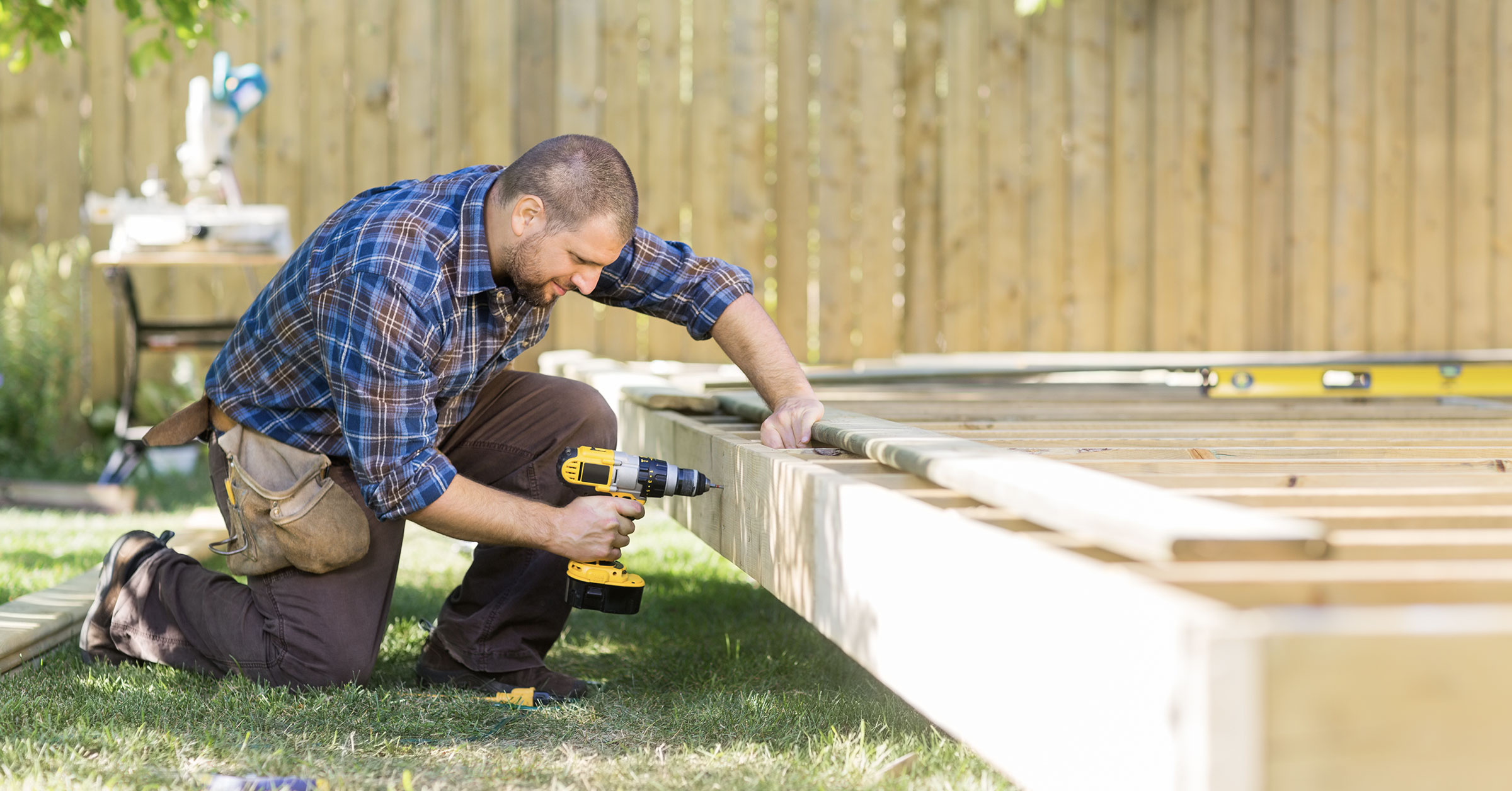 An image of a professional expertly building a wooden deck using a drill and other tools.